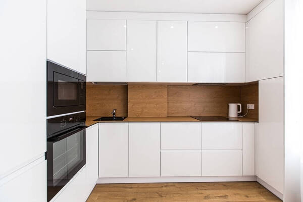 Minimalista, fehér magasfényű konyhabútor fa munkalappal és beépített konyhagépekkel – egy elkészült budapesti projekt a Bízd Ránk Lakásfelújítás 2026 kivitelezésében.